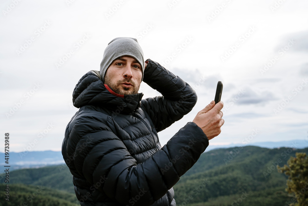 Male tourist at viewpoint holding smart phone against sky during winter Male tourist at viewpoint holding smart phone against sky during winter