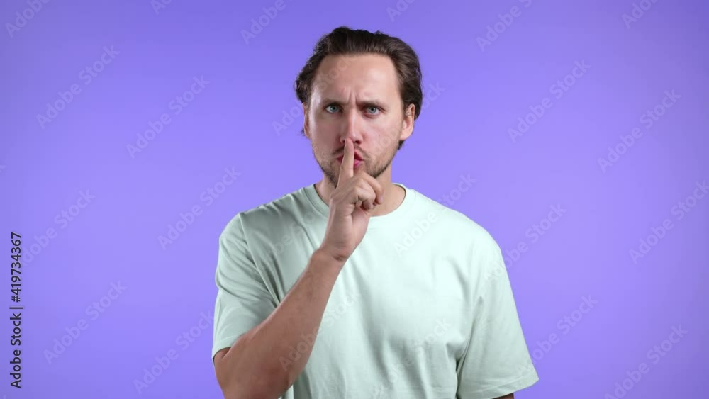 Serious man holding finger on lips over violet background. Gesture of shhh, secret, silence. Close up. Serious man holding finger on lips over violet background. Gesture of shhh, secret, silence. Close up.