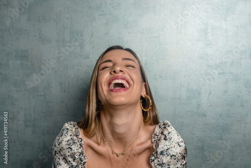 Close-up of beautiful woman with eyes closed laughing against concrete wall photo