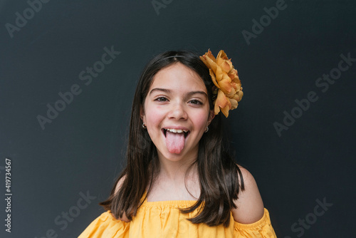Close-up of girl wearing yellow headband sticking out tongue against black background