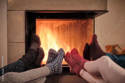 Family warming up feet in woolen socks by fireplace in living room photo