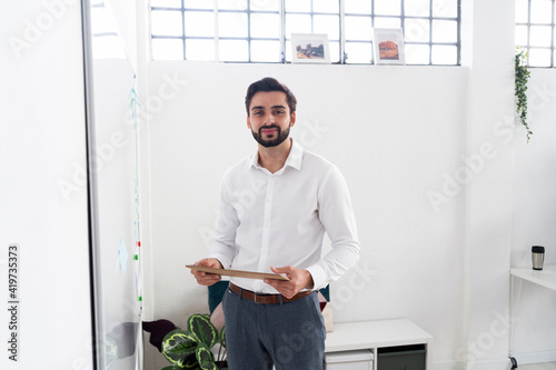 Smiling male professional holding clipboard while standing by whiteboard in office