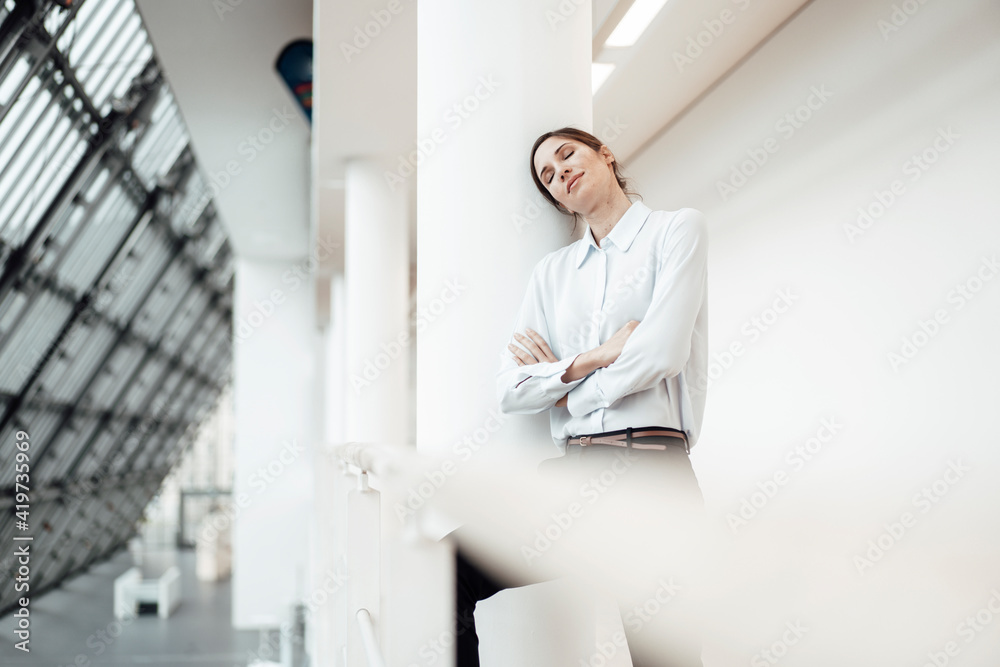 Female entrepreneur with eyes closed leaning by wall in corridor at office Female entrepreneur with eyes closed leaning by wall in corridor at office