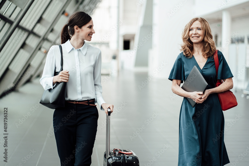 Smiling female professionals discussing while walking in corridor at office