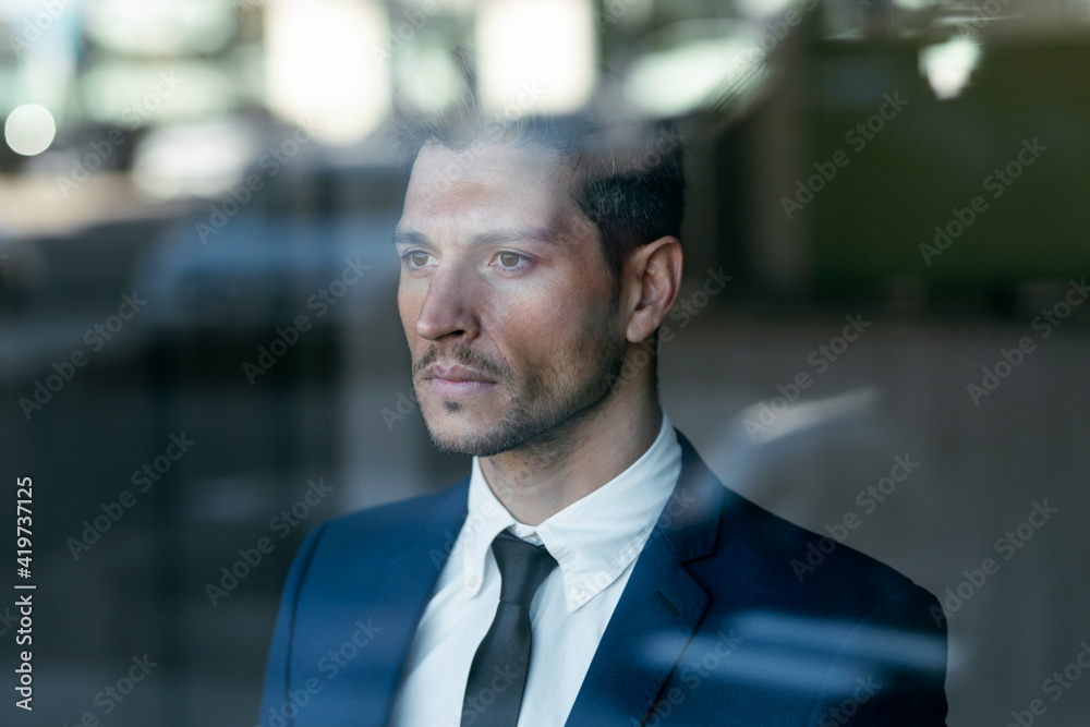Thoughtful businessman looking through glass window while standing in office Thoughtful businessman looking through glass window while standing in office