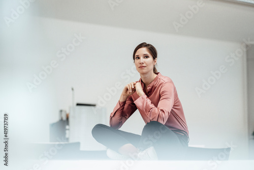 Thoughtful businesswoman with cross legged sitting in office