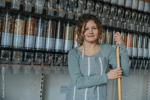 Smiling saleswoman standing with stick against food dispenser in retail store photo