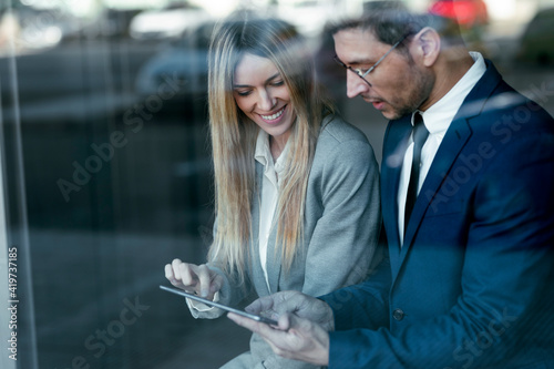 Businessman having discussion over digital tablet with colleague while standing in office photo