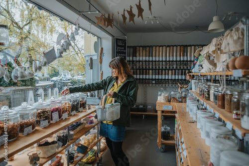 Mature woman shopping groceries from glass jar in zero waste shop photo