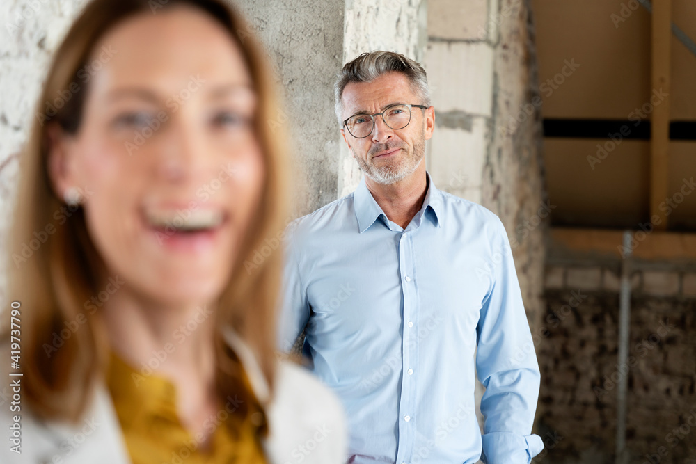 Mature architect staring while standing with businesswoman at construction site Mature architect staring while standing with businesswoman at construction site