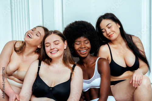 Happy multi-ethnic group of models in lingerie with eyes closed sitting against white wall photo