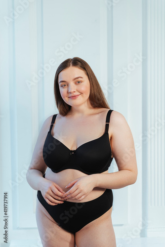 Beautiful plus size model in lingerie standing against white wall