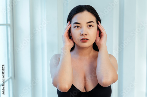 Plus size model with hand in hair wearing black bra against white wall photo