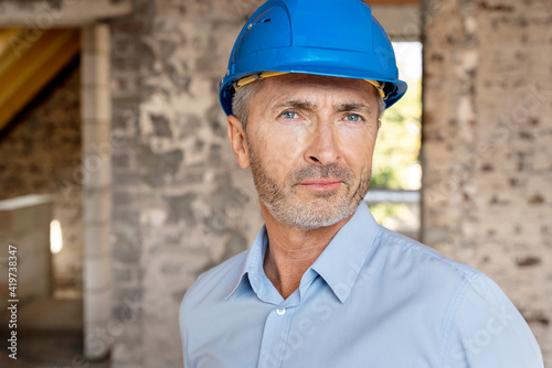 Confident architect wearing hardhat staring while standing at construction site photo