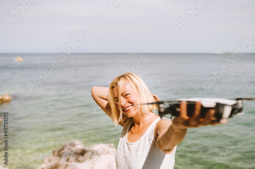 Smiling woman holding drone while standing against sea
