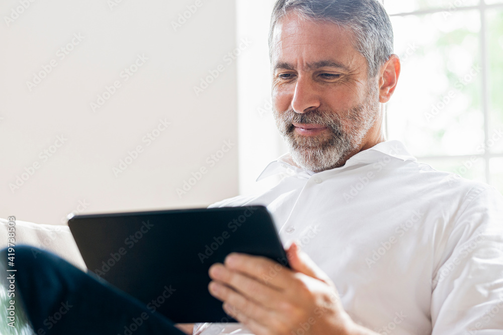 Smiling businessman working on digital tablet while sitting at home Smiling businessman working on digital tablet while sitting at home