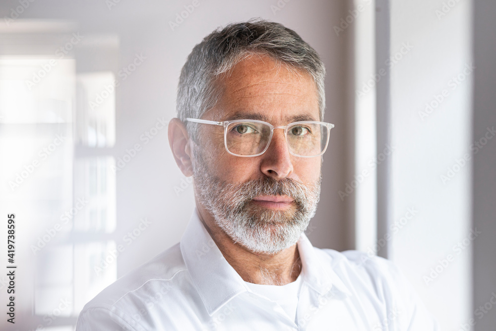 Confident businessman wearing eyeglasses staring while standing at home Confident businessman wearing eyeglasses staring while standing at home