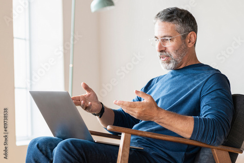 Mature businessman talking on video call through laptop while sitting at home photo