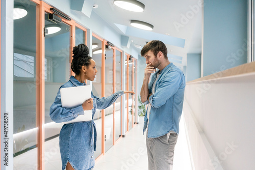 Young businesswoman with laptop arguing with male colleague in corridor at workplace photo