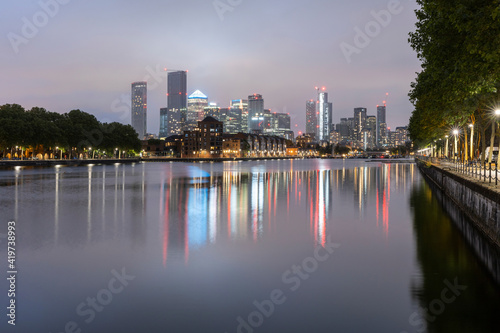 Illuminated skyscrapers reflecting on Thames river against clear sky at dusk, Canary Wharf, London, UK