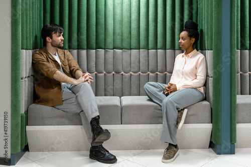 Creative male and female colleagues discussing while sitting on sofa at work place