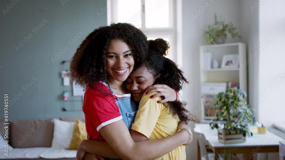 Portrait of young sisters hugging indoors at home, looking at camera. Portrait of young sisters hugging indoors at home, looking at camera.