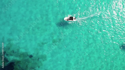 Descending vertical aerial tracks motorboat in clear shallow water photo