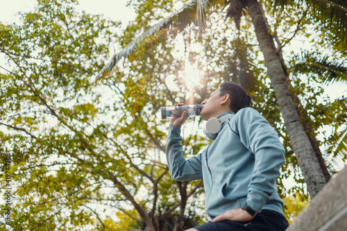 Young sport man drink water after jogging, running in the park. Sport thirsty and resting after exercise. © Charnchai saeheng