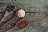 Red, black and white quinoa seeds in different spoons over  black slate stone background. Top view. 
