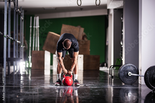 Muscular athlete power lifting a kettlebell. Man working out indoors