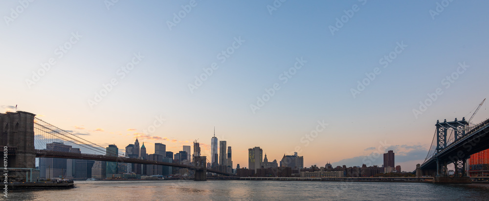 Wide panorama image of Manhattan Skyscrapers and Brooklyn bridge at dusk in New York, USA