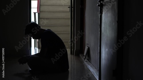 Silhouette of a stressed man sitting in the dark leaning against on steps in old condo, lost in life, violence, The concept of depression and suicide.
