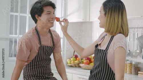 Happy Asian beautiful young family couple husband and wife enjoying smile and laugh  woman hold the strawberry to the man s nose spending time together in kitchen at home.