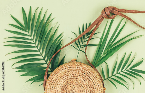Tropical palm leaves, straw bag on green background. Trendy tropical pattern. Fashion clothing and accessories. Flat lay. Summer, vacation, holidays concept. 