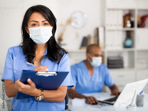 Tableau sur toile Portrait of female therapist in protective mask with folder for papers in clinic