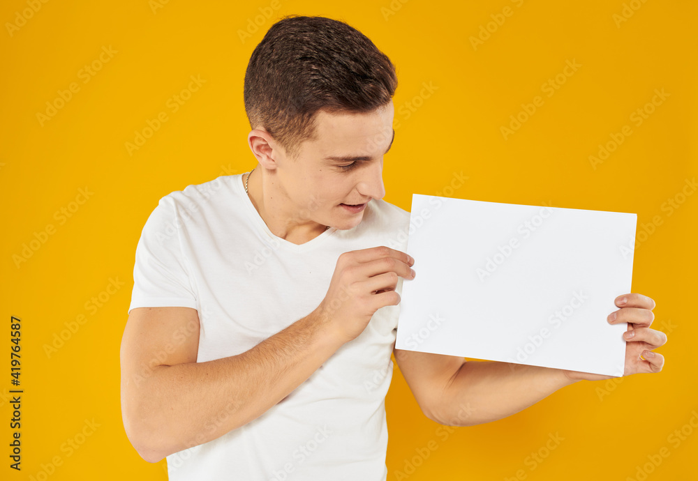 A man on a yellow background with a mockup in his hand a white sheet of paper A man on a yellow background with a mockup in his hand a white sheet of paper
