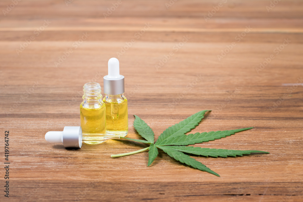 Cannabis oil extracts in dropper bottle and cannabis leaf on wooden background Cannabis oil extracts in dropper bottle and cannabis leaf on wooden background