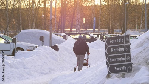 Swedish old man with walker make way through snow-capped landscape - Wide tracking shot photo