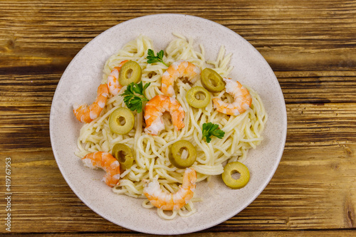 Spaghetti pasta with prawns, green olives and parsley on wooden table. Top view