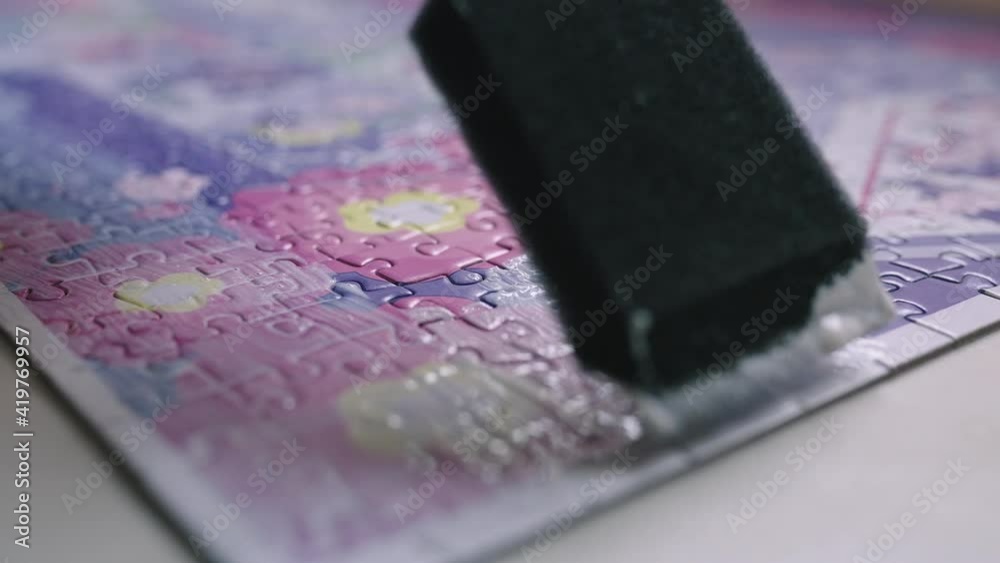 The hobbyist paints a puzzle with mod podge glue. The hobbyist paints a puzzle with mod podge glue.