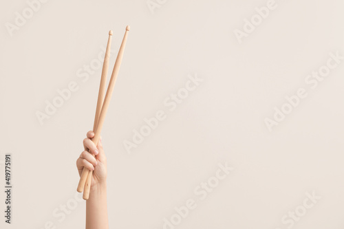 Woman holding wooden drumsticks on color background