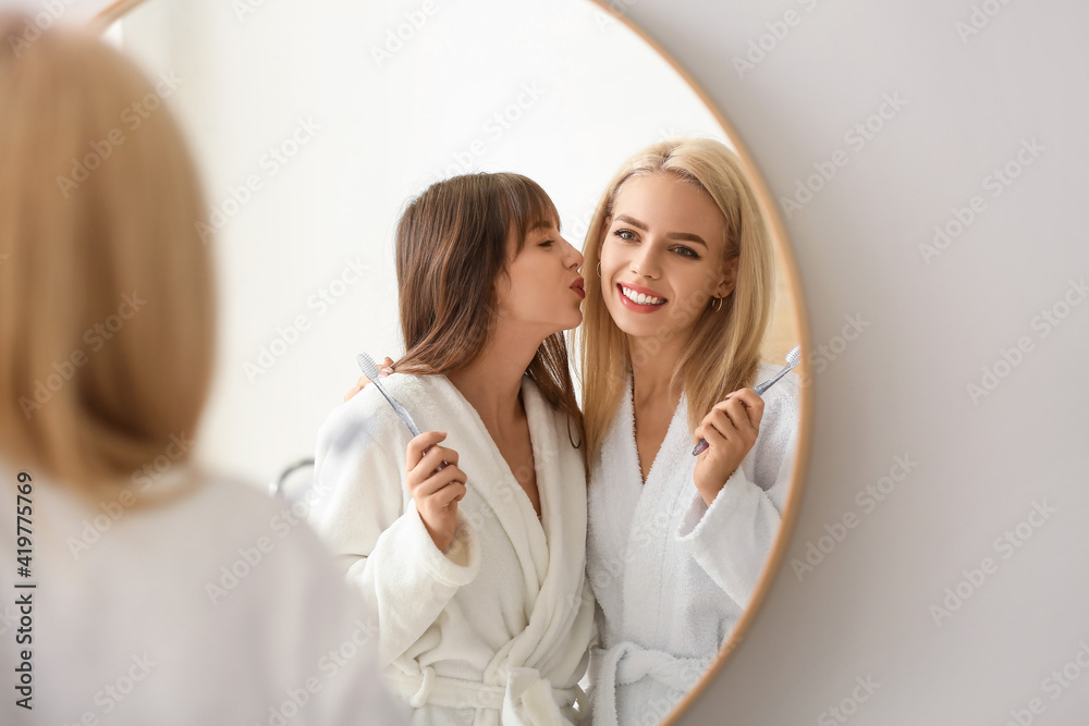 Happy lesbian couple brushing teeth in bathroom Happy lesbian couple brushing teeth in bathroom