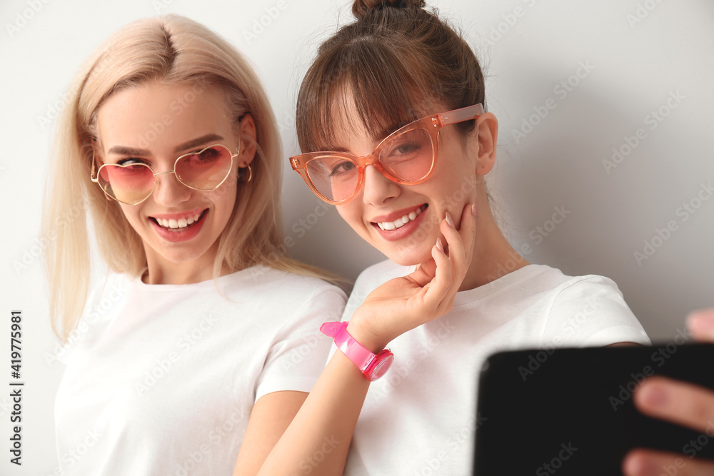 Young lesbian couple taking selfie on light background Young lesbian couple taking selfie on light background
