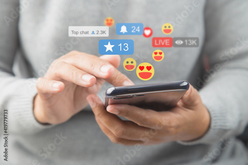 Close-up of a woman in a soft shirt using the smart phone, hands holding and typing to communicate with others through emoji and text online.