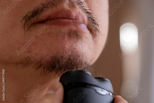 Asian man shakes his beard using an electric shaver