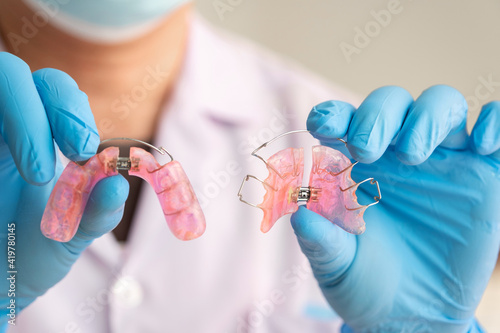Dentist in rubber gloves is holding a dental device Removable braces for children with crooked teeth photo