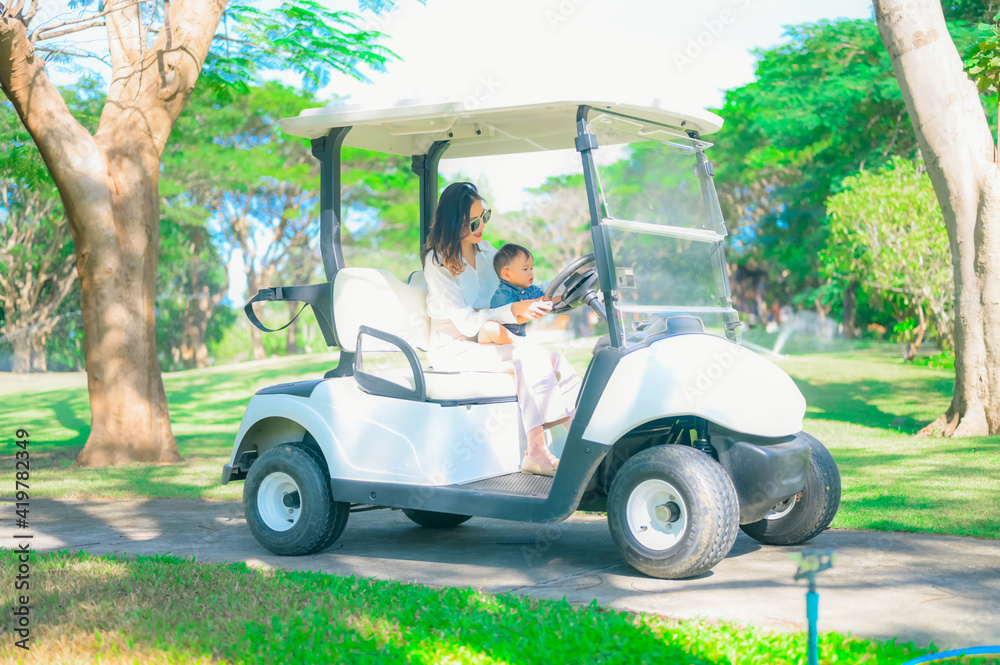 A woman is sitting at the wheel of a golf car, the son is sitting next to the passenger seat.