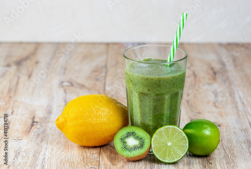 Tall glass with kiwi and spinach smoothie surrounded by fruits on a wooden table