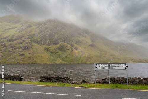 Road signs Leenaun and Louisburgh by a road. Beautiful scenery in the background. Mountains and low clouds and a lake. Connemara, Ireland photo