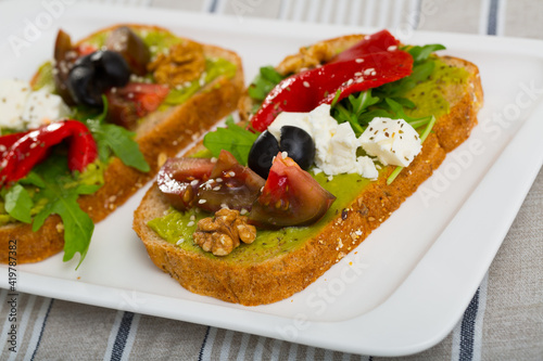 Slices of bread with guacamole and soft cheese decorated with fresh vegetables, herbs and walnut.
